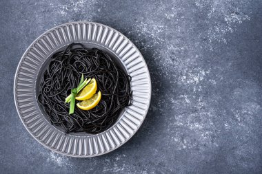 Üst görünüm, mürekkep balığı mürekkebi ve limon dilimleri içeren siyah makarna. Gri arka planda gri tabakta, kopyalama alanı olan yaprak.