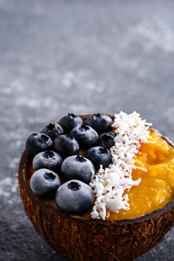 Yabanmersinli smoothie kasesi, donmuş mango püresi ve Hindistan cevizi ezmesi, gri arka planda.