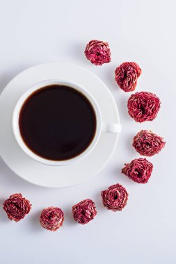 Beyaz bardakta, beyaz fonda gül tomurcuklarıyla süslenmiş siyah kahve, sanat kahvesi konsepti.