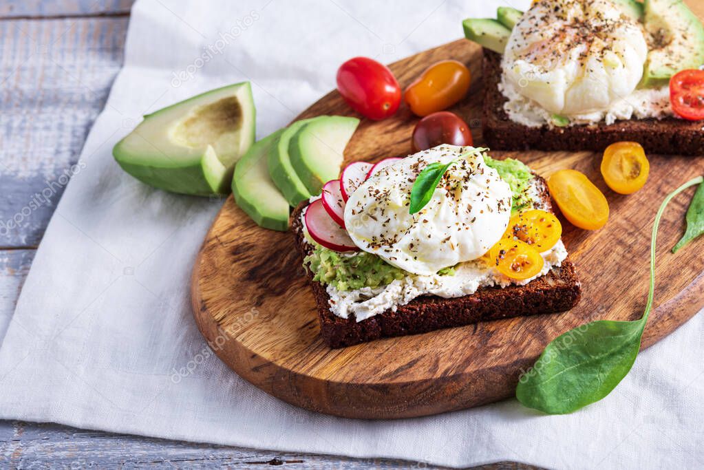 closeup vegetarian toast with poached eggs, cottage cheese, avocado and vegetables on wooden Board