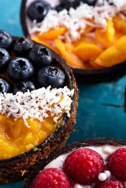 Meyve ve meyveli düşey meyve suyu kaseleri, mavi arka planda hindistan cevizi kasesinde egzotik tatlı şerbeti.