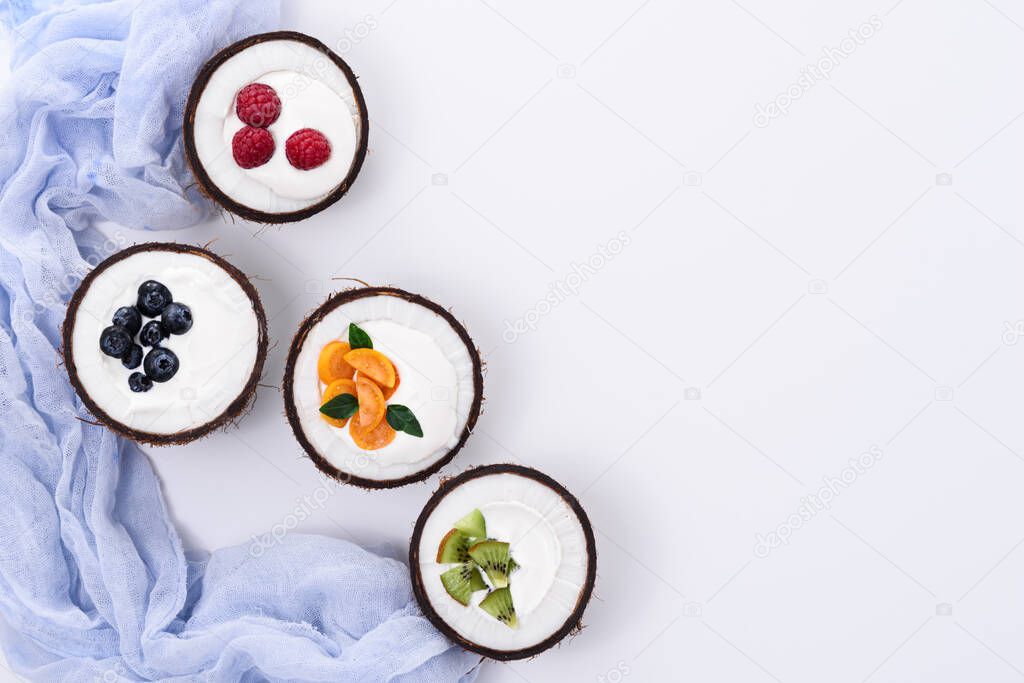 top view four ice cream with fruit and berry, yogurt in coconut bowls on white background with blue towel, trendy dessert concept