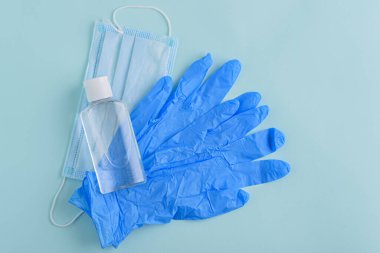 Üst görüş dezenfektanı, tıbbi eldivenler, mavi arka planda tıbbi maske, koruyucu ekipman konsepti, karantina, kendini izole etme