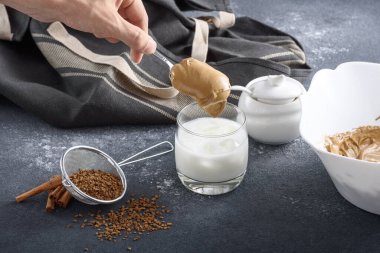 Dalgona kahvesi yapma süreci, Kore içkisi gri mutfak masasında, eller süt bardağına köpük koyar, yakın plan.