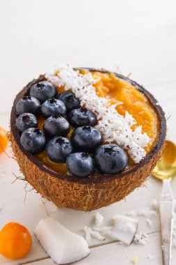 Mangolu smoothie kasesi, yaban mersini ve hindistan cevizi talaşı beyaz arka planda hindistan cevizi kaseleri, mango şerbeti, yakın plan