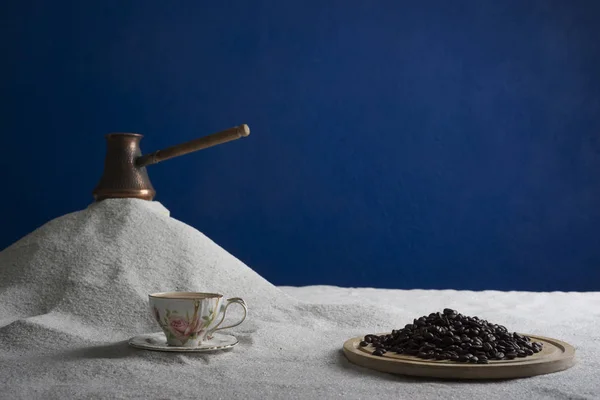 Bir fincan kahve ve kahve üzerinde mavi bir arka plan üzerinde beyaz kum taneleri