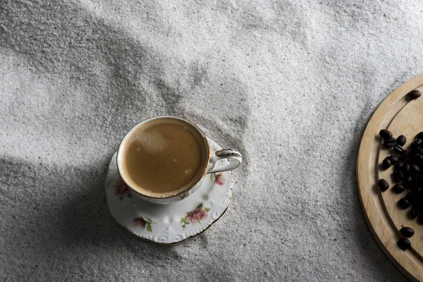 Bir fincan kahve ve kahve üzerinde mavi bir arka plan üzerinde beyaz kum taneleri