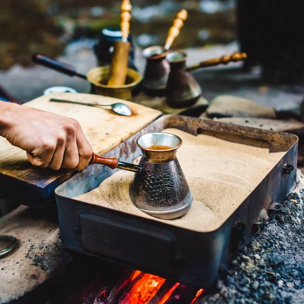 El hombre está cocinando café turco en la caja con arena bajo carbones vivos Imagen de stock
