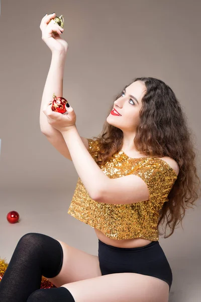 Joven hermosa chica en un vestido de oro con bolas de Navidad y juguetes rojos de Navidad — Foto de Stock