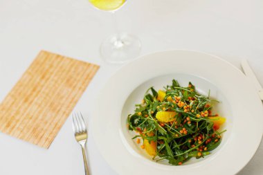 Beyaz tabakta roka salatası, portakal fileto ve mercimek. 