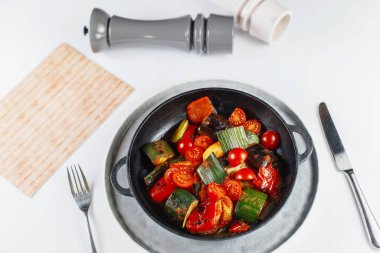 Menünün yanındaki beyaz masada sebze tavası, tuz ve biber.