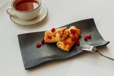 Siyah tabakta kirazlı gözleme ve bir fincan çay.