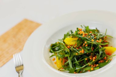 Beyaz tabakta roka salatası, portakal fileto ve mercimek. 