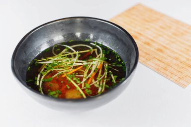 Siyah tabakta Asya çorbası, menünün yanında.