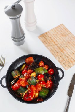 Menünün yanındaki beyaz masada sebze tavası, tuz ve biber.