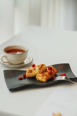 Siyah tabakta kirazlı gözleme ve bir fincan çay.