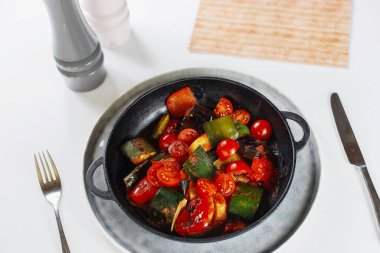 Menünün yanındaki beyaz masada sebze tavası, tuz ve biber.