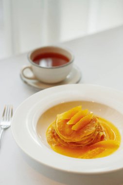 Beyaz tabakta portakallı krep ve çay.