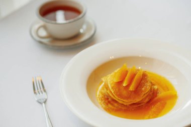 Beyaz tabakta portakallı krep ve çay.