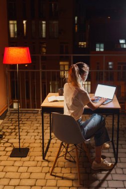 Genç yorgun kadın terasta dizüstü bilgisayar kullanıyor.