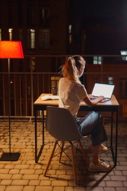 Genç yorgun kadın terasta dizüstü bilgisayar kullanıyor.