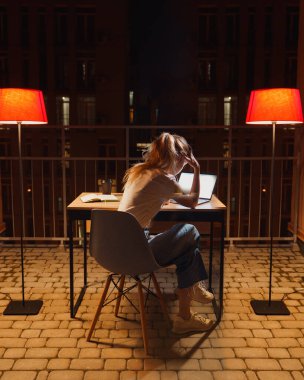 Genç yorgun kadın terasta dizüstü bilgisayar kullanıyor.