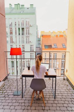 Genç yorgun kadın terasta dizüstü bilgisayar kullanıyor.