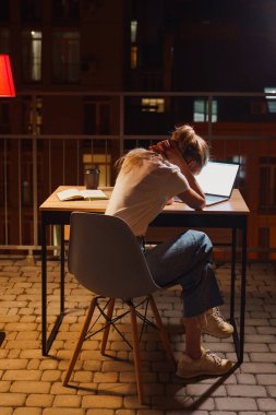 Genç yorgun kadın terasta dizüstü bilgisayar kullanıyor.