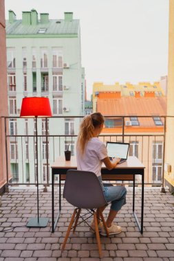 Genç yorgun kadın terasta dizüstü bilgisayar kullanıyor.