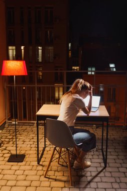 Genç yorgun kadın terasta dizüstü bilgisayar kullanıyor.