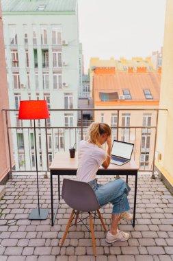 Genç yorgun kadın terasta dizüstü bilgisayar kullanıyor.