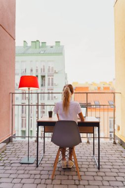 Genç yorgun kadın terasta dizüstü bilgisayar kullanıyor.