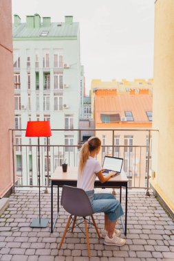 Genç yorgun kadın terasta dizüstü bilgisayar kullanıyor.
