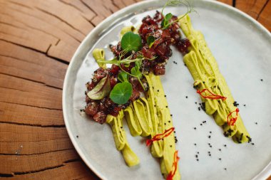 Siyah havyarlı ton balığı tartartarı, avokado mus, kırmızı biber, susam tohumu, roka, pazı ve ahşap arka planda mikroyeşil.