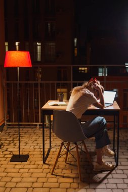 Genç yorgun kadın terasta dizüstü bilgisayar kullanıyor.