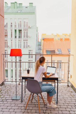 Genç yorgun kadın terasta dizüstü bilgisayar kullanıyor.