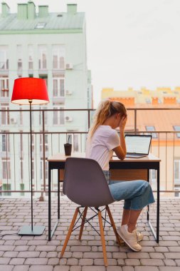 Genç yorgun kadın terasta dizüstü bilgisayar kullanıyor.