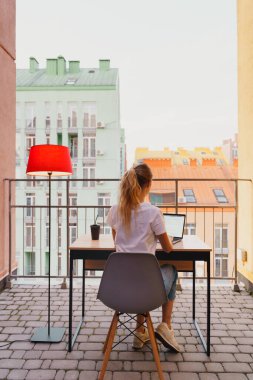 Genç yorgun kadın terasta dizüstü bilgisayar kullanıyor.