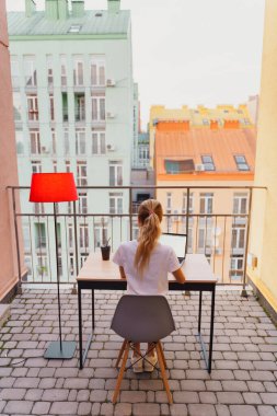 Genç yorgun kadın terasta dizüstü bilgisayar kullanıyor.