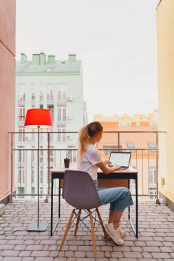 Genç yorgun kadın terasta dizüstü bilgisayar kullanıyor.