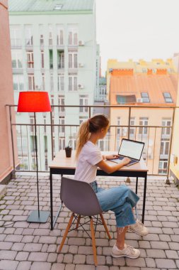 Genç yorgun kadın terasta dizüstü bilgisayar kullanıyor.