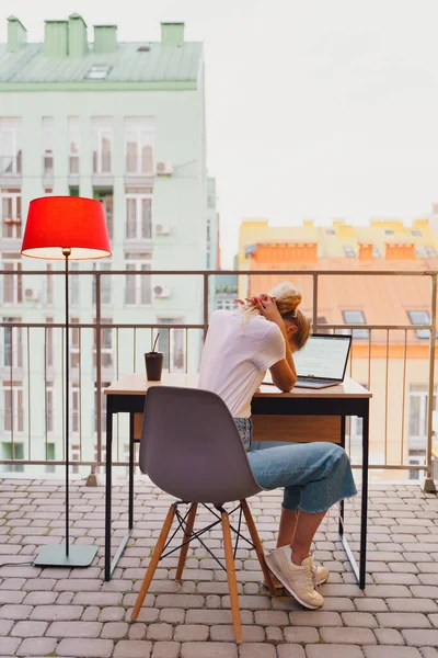 Genç yorgun kadın terasta dizüstü bilgisayar kullanıyor.