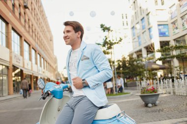 Mavi elbiseli genç adam şehirde mobiletle poz veriyor.