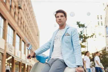 Mavi elbiseli genç adam şehirde mobiletle poz veriyor.