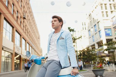 Mavi elbiseli genç adam şehirde mobiletle poz veriyor.