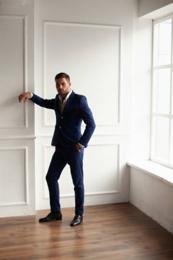 Pencere kenarında poz veren ceketli genç adam. 