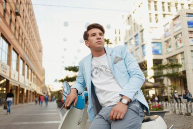 Mavi elbiseli genç adam şehirde mobiletle poz veriyor.