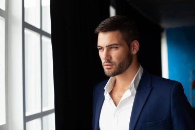 Pencere kenarında poz veren ceketli genç adam. 