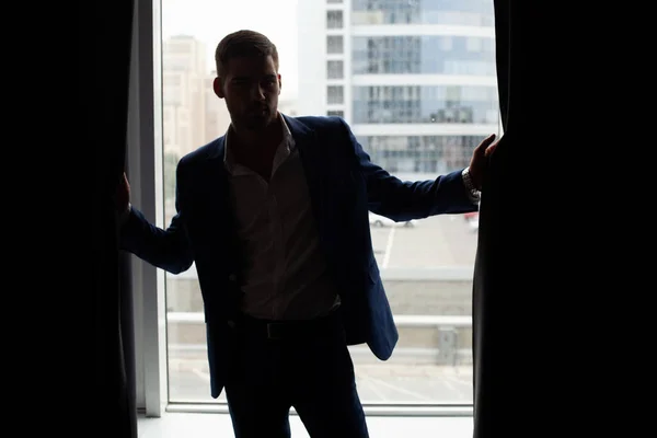 young man wearing jacket posing by window