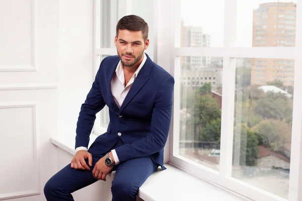 young man wearing jacket posing by window